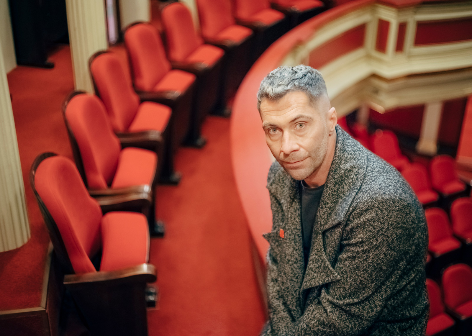 A middle-aged man with graying hair sits in front of a theater audience - conversation graphic