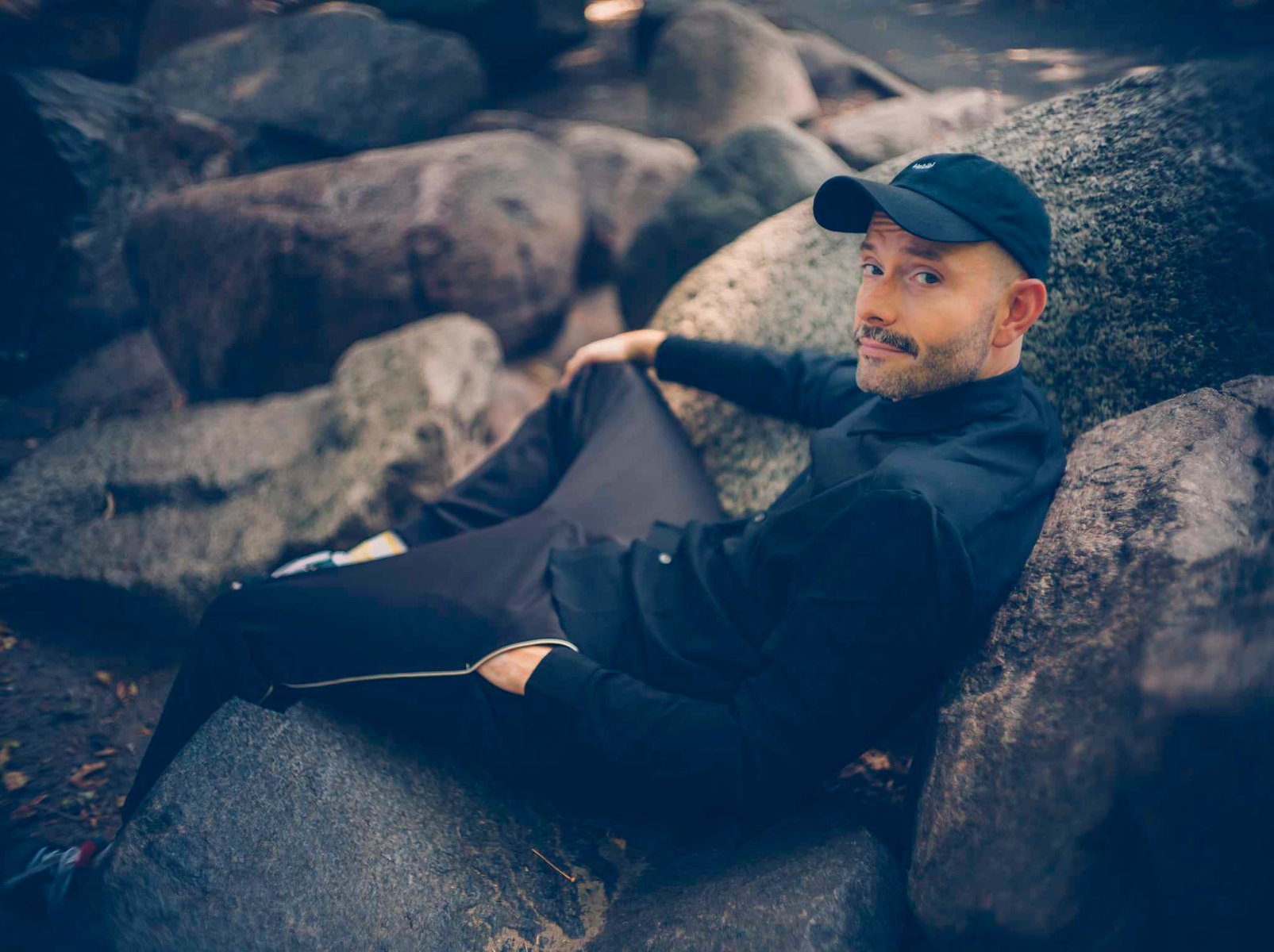 young man with moustache sitting on rocks - conversation graphic