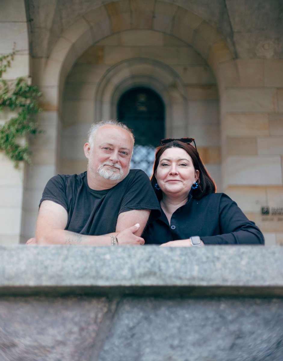 a man with gray hair and a beard and a woman with dark hair stand next to each other - conversation graphic