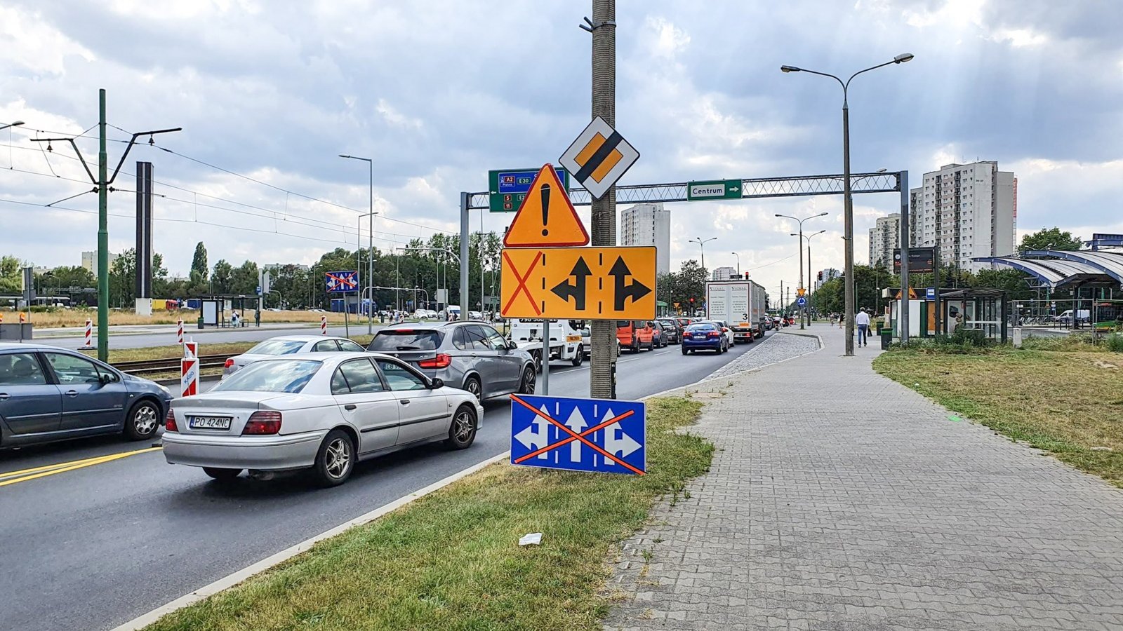 Na zdjęciu znajduje się jezdnia, po której jadą samochody oraz chodnik. W tle widać Dworzec Rataje