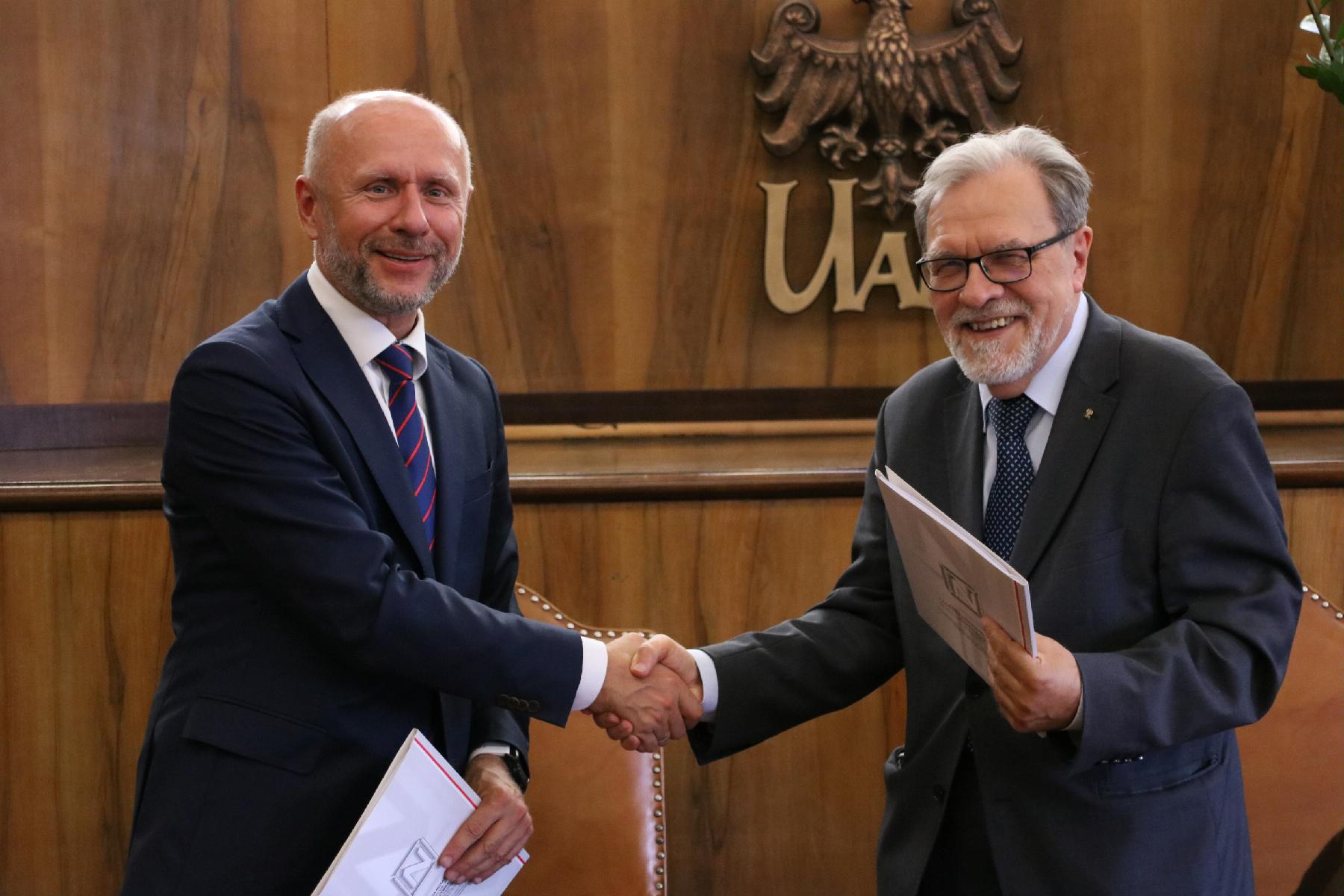 Na zdjęciu znajdują się rektor UAM Andrzej Lesicki i Bartosz Guss, wiceprezydent Poznania. Panowie podają sobie dłonie - grafika rozmowy