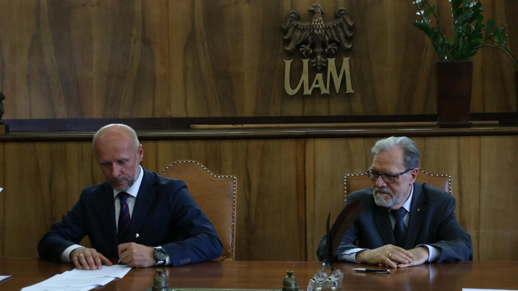 Przy stole siedzą rektor UAM Andrzej Lesicki i Bartosz Guss, wiceprezydent Poznania. Wiceprezydent podpisuje dokumenty
