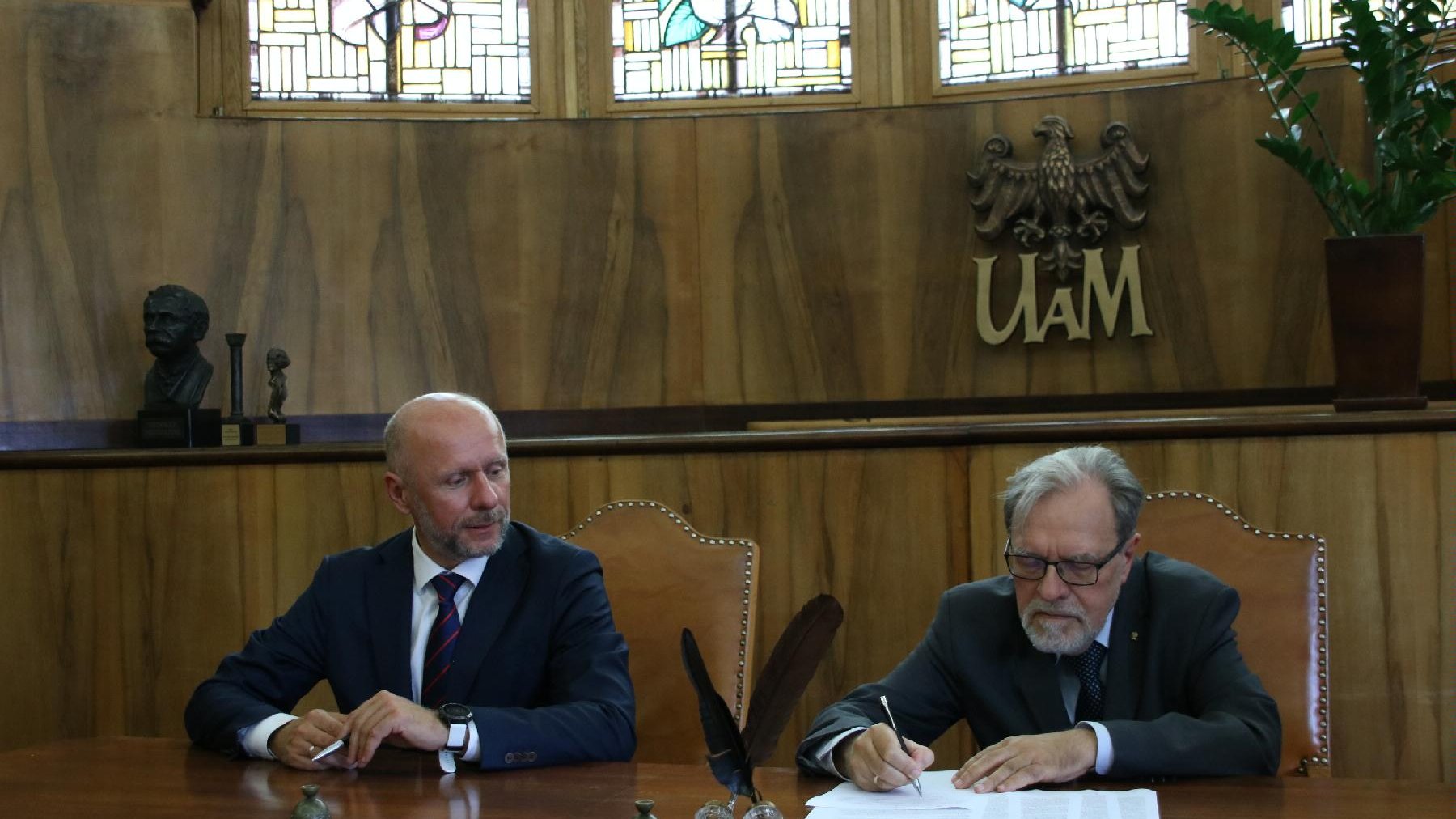 Przy stole siedzą rektor UAM Andrzej Lesicki i Bartosz Guss, wiceprezydent Poznania. Rektor podpisuje dokumenty
