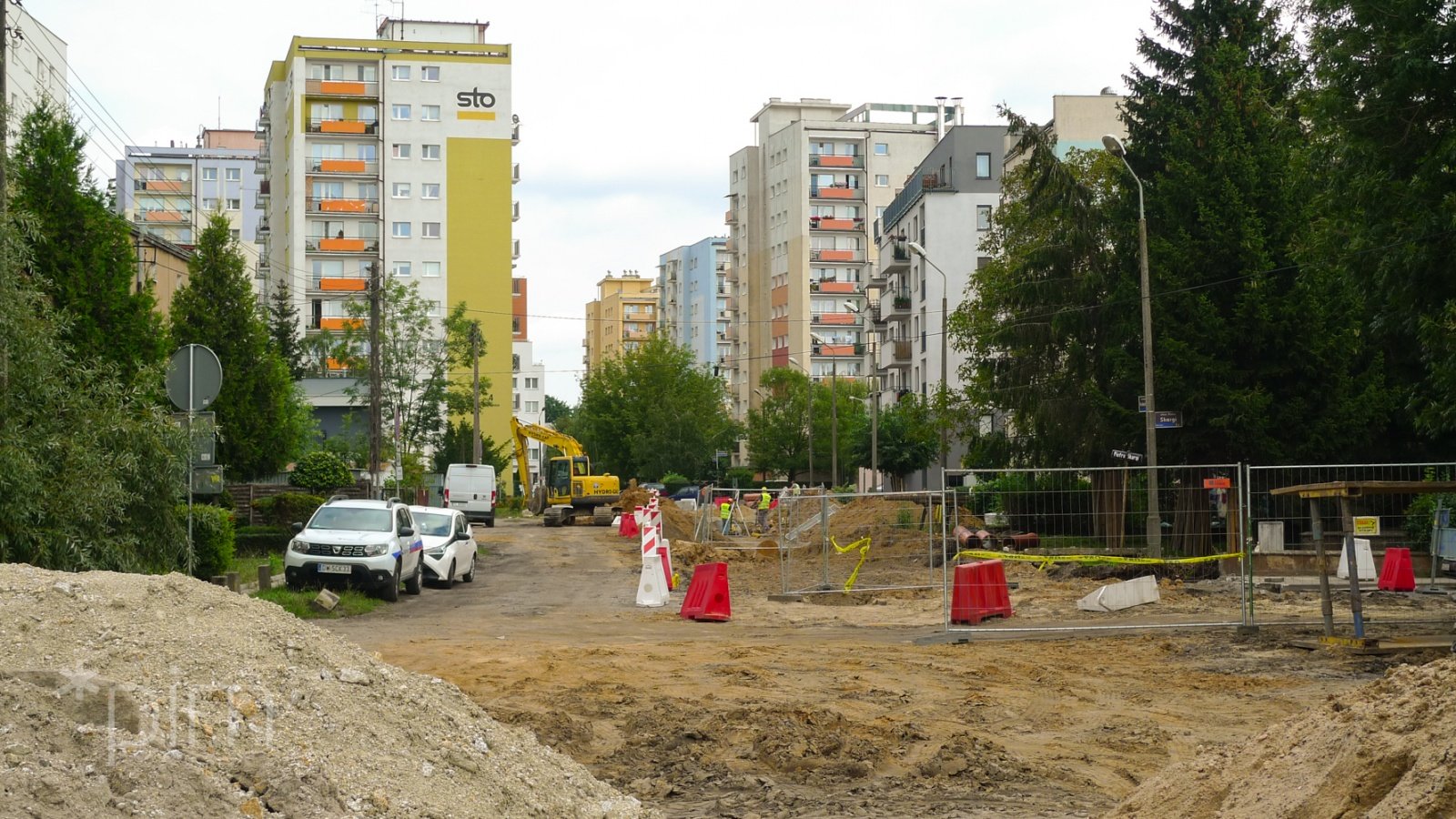 Rozkopana ulica Kordeckiego. Po obu stronach widać drzewa. W tle wysokie bloki