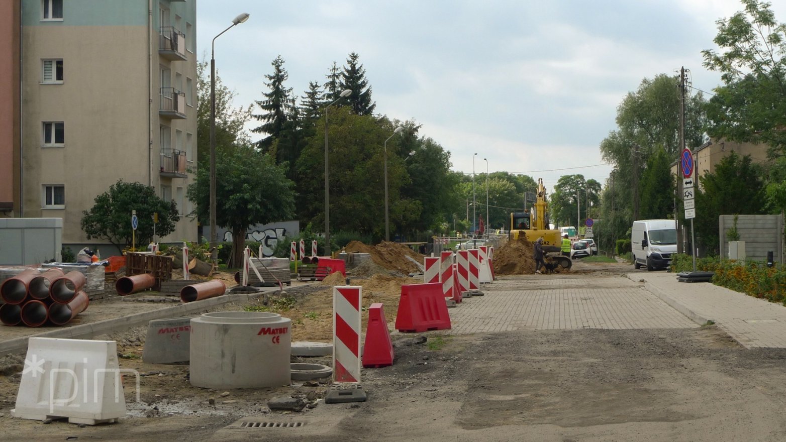 Po lewej stronie rozkopana ulica Kordeckiego i blok. W tle drzewa i maszyny budowlane