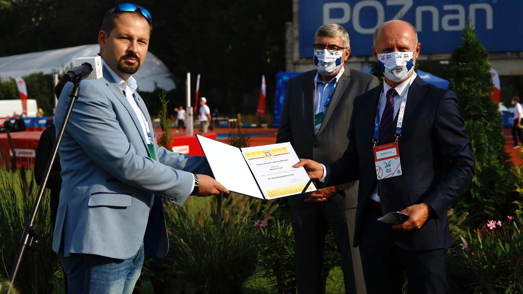 Przedstawiciel PZLA wręcza Bartoszowi Gussowi certyfikat przyznania Poznaniowi organizację Mistrzostw Polski w lekkoatletyce w 2021. Na drugim planie Grzegorz Ganowicz, przewodniczący Rady Miasta