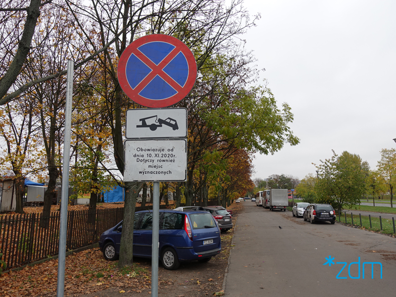 Znaki informujące o zakazie zatrzymywania i zaparkowane samochody w okolicach targowiska. - grafika rozmowy