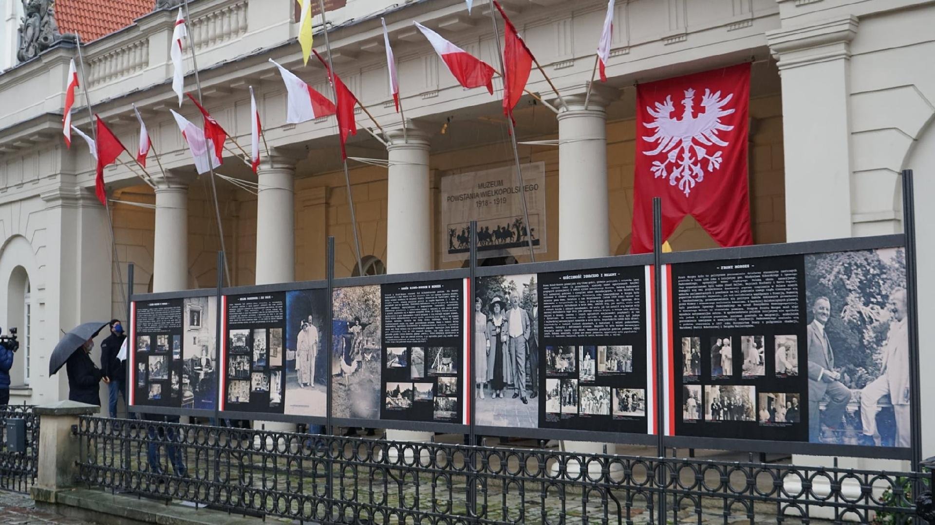 Stary Rynek: na pierwszym planie widzimy budynek muzeum, przed nim znajdują się tablice ze zdjęciami Paderewskiego. Wystawę oglądają przechodnie z parasolami.