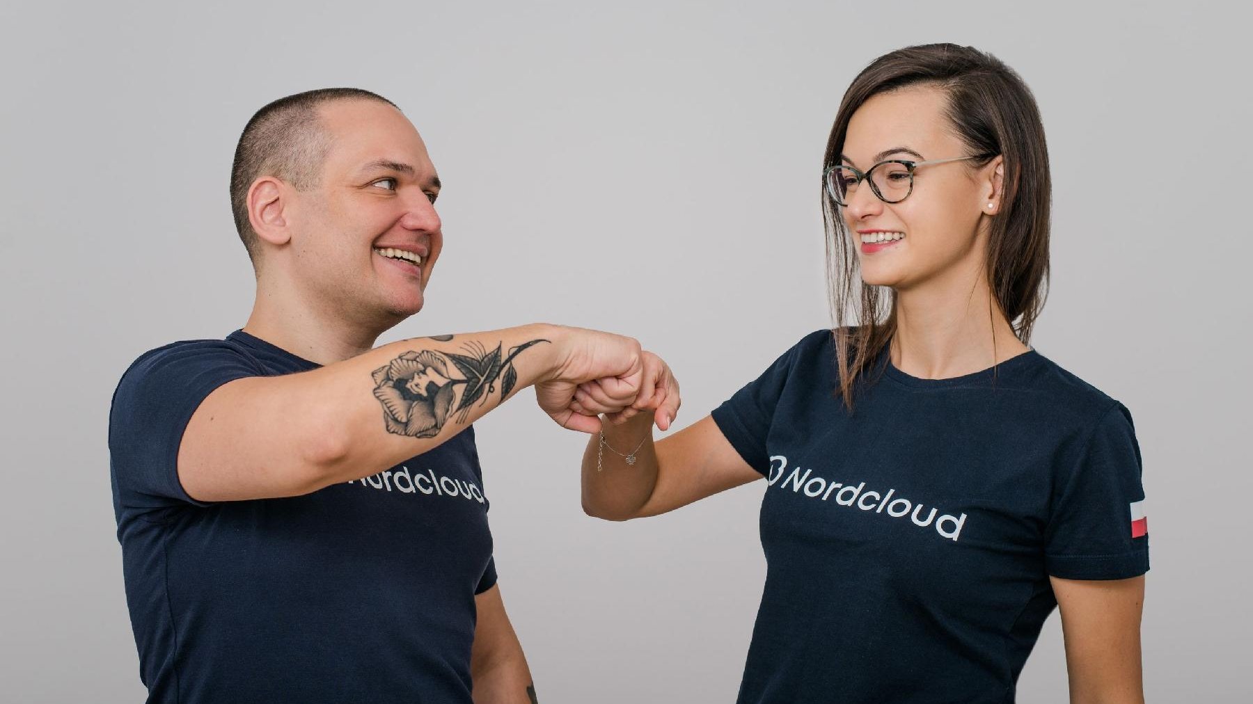 Mężczyzna i kobieta ubrani w koszulki z napisem Nordcloud przybijają sobie żółwika