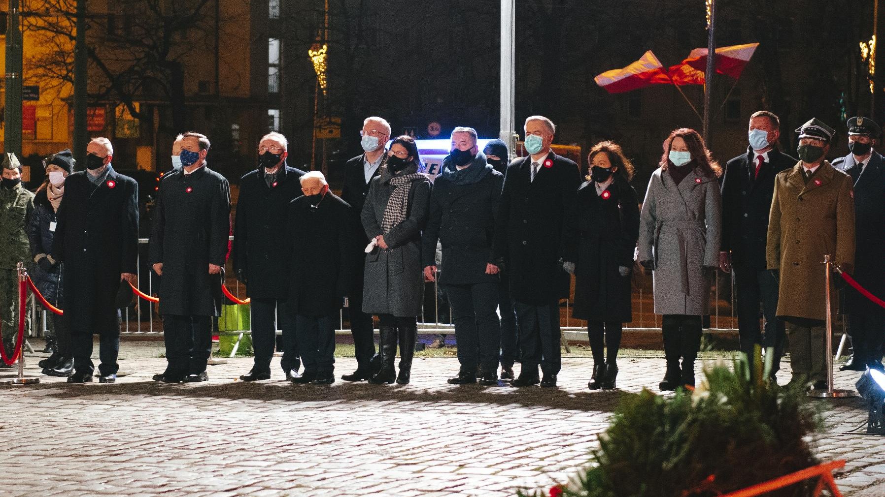 Na pierwszym planie wieniec kwiatów. W tle uczestnicy obchodów.