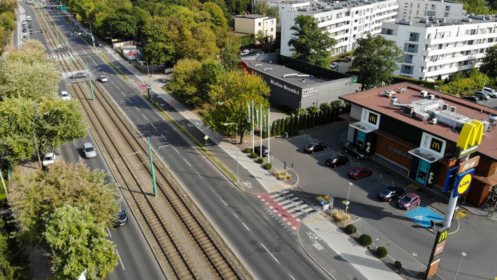 Zdjęcie przedstawia jezdnię z torowiskiem i drogą rowerową widzianą z góry. Po prawej stronie znajdują się zabudowania.