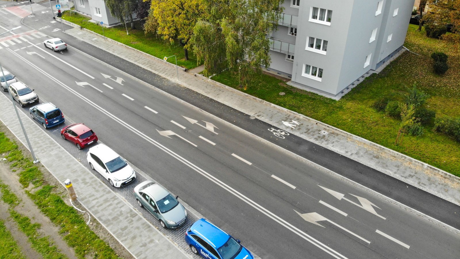 Jezdnia z drogą rowerową widziana z góry. Obok stoją zaparkowane samochody.