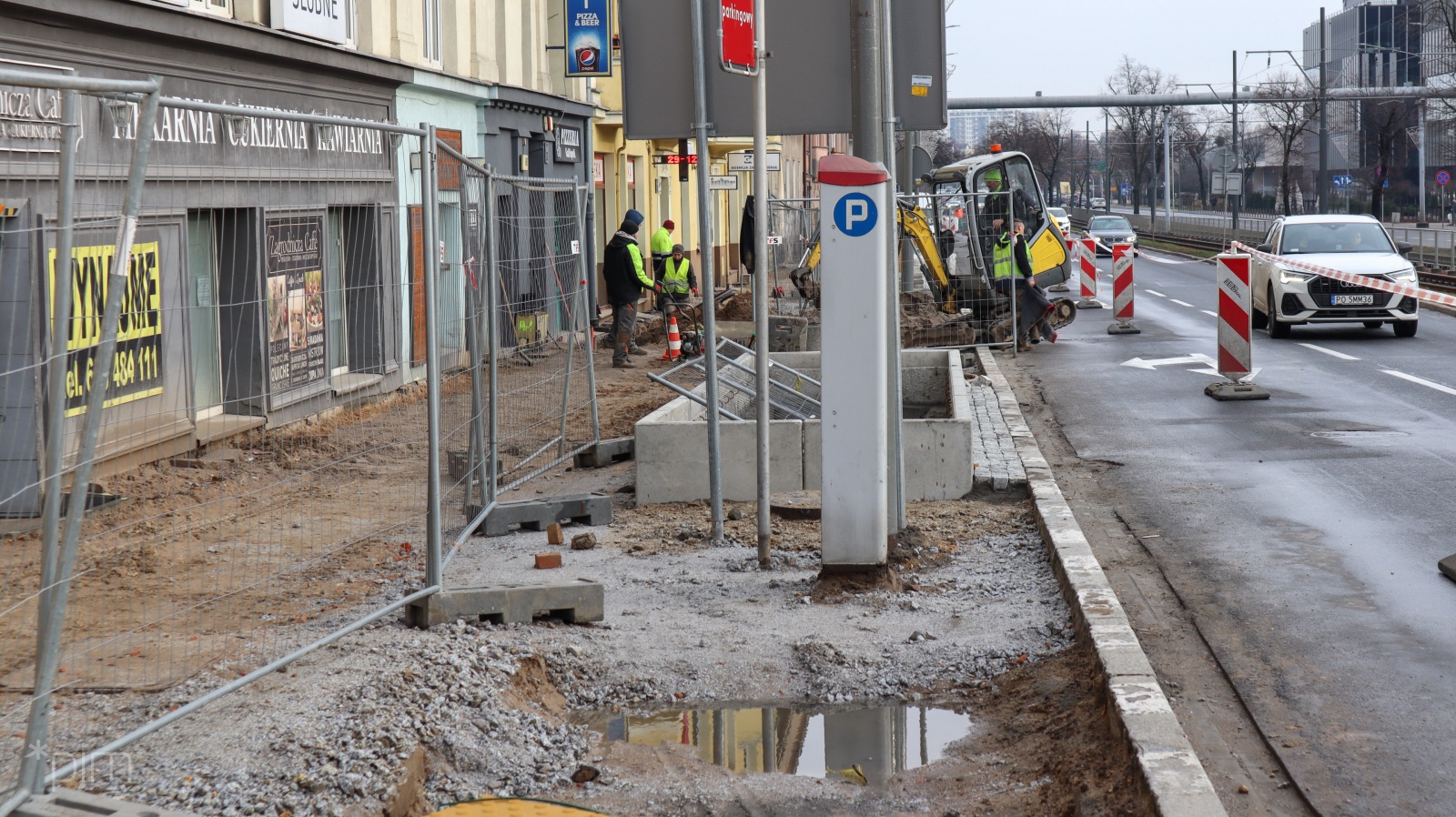 Pracownicy budowlani układają nawierzchnię chodnika. Na zdjęciu widać też jezdnię i samochody. - grafika rozmowy