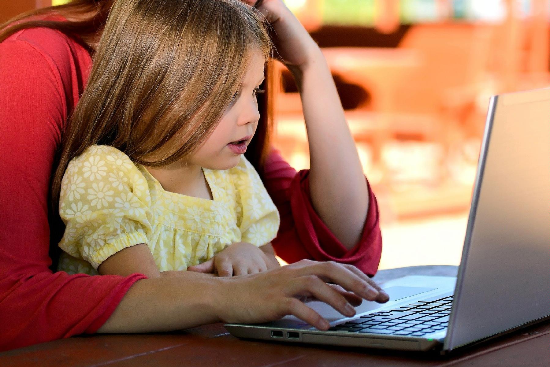 Zdjęcie przedstawia dziecko siedzące na kolan rodzica. Dziecko patrzy na ekran laptopa. - grafika rozmowy