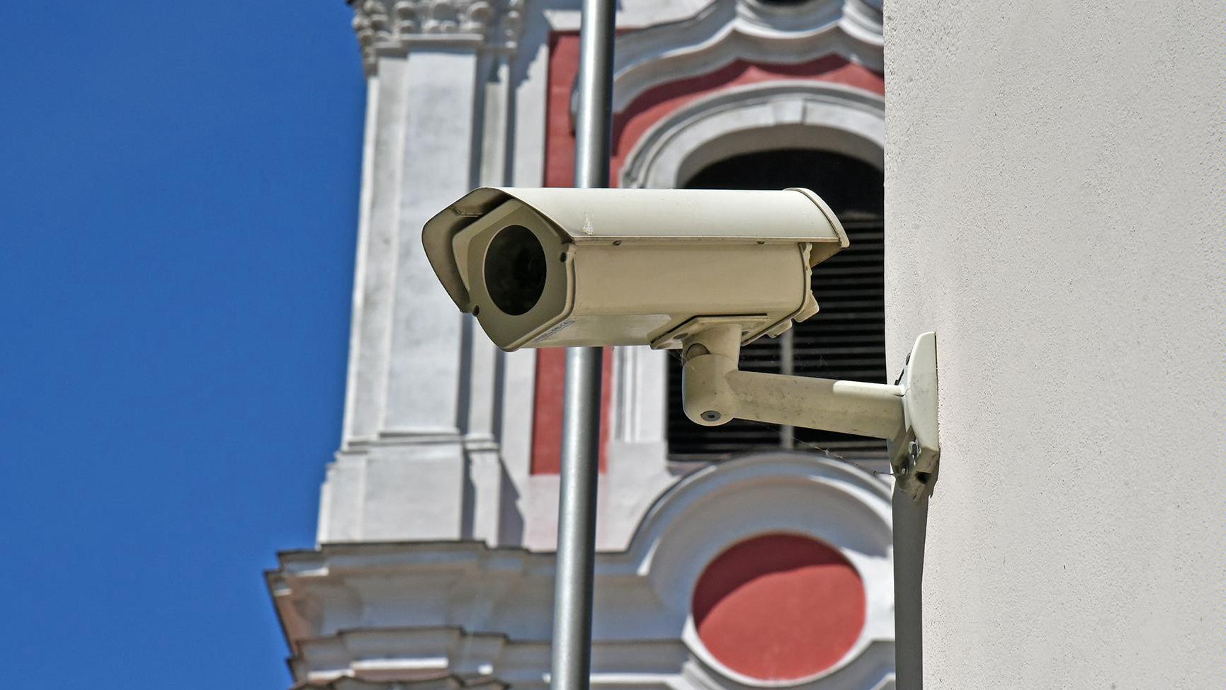 Zdjęcie przedstawia kamerę, zamontowaną na budynku urzędu przy placu Kolegiackim. Fotografia ukazuje zbliżenie na kamerę. - grafika rozmowy