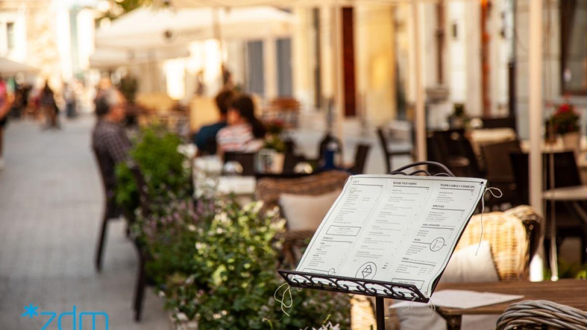 Zdjęcie ogródka gastronomicznego, na pierwszym planie wystawiona karta dań - grafika rozmowy