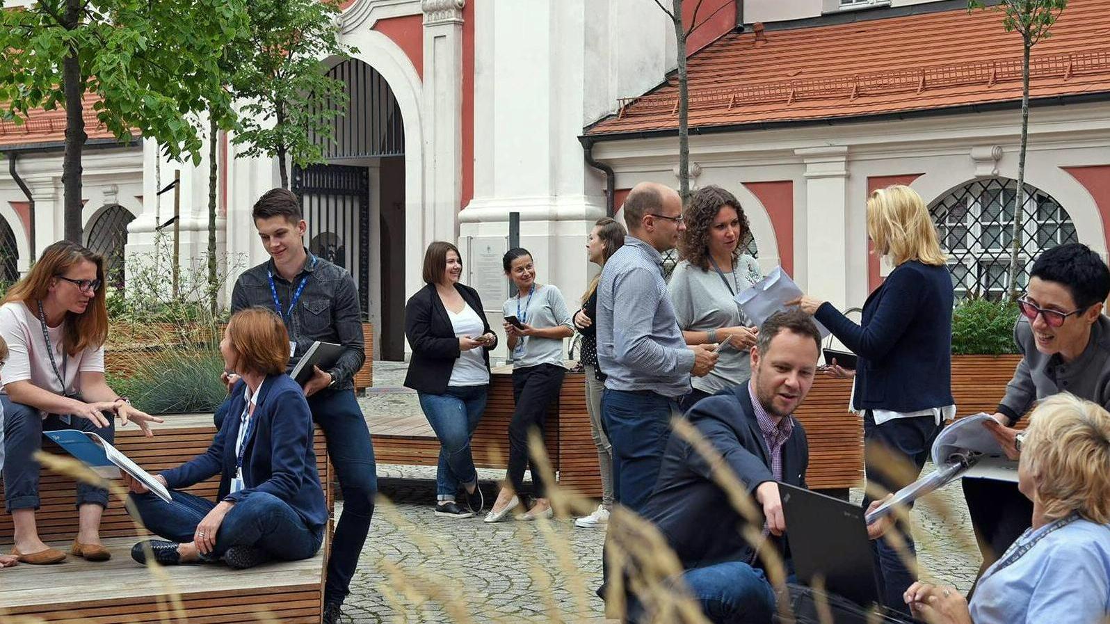 Dziedziniec Urzędu Miasta Poznania - na zdjęciu widzimy wielu ludzi, którzy połączyli się w małe grupki, śmieją się i rozmawiają. - grafika rozmowy