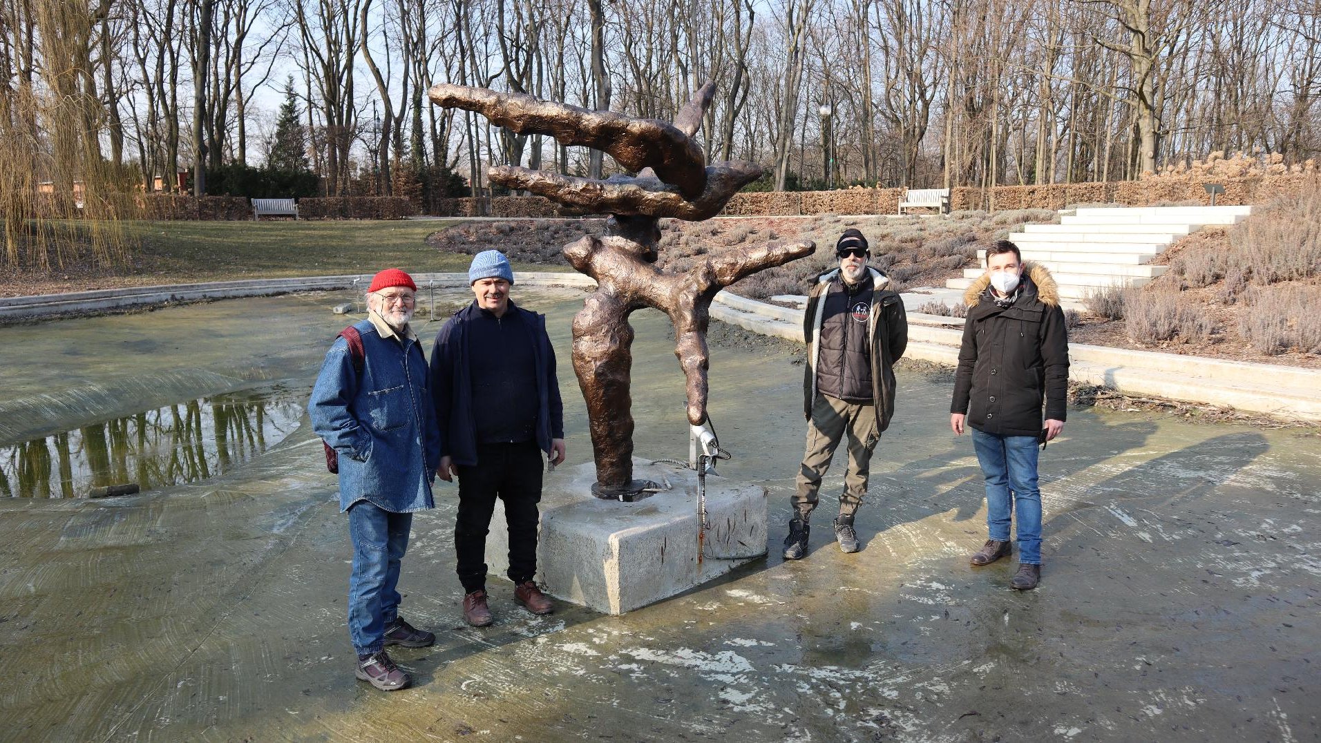 Czterech mężczyzn pozuje do zdjęcia przy rzeźbie. W tle widać park w jesiennej odsłonie.