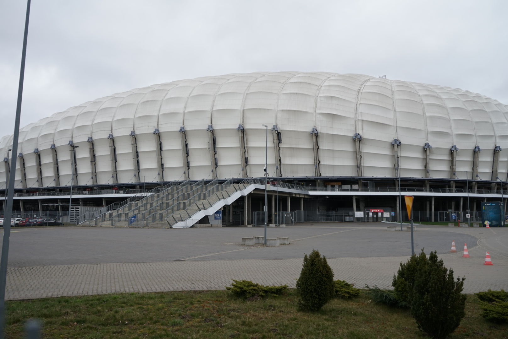 Zdjęcie stadionu, w centrum schody prowadzące do wewnątrz budynku, na pierwszym planie rośliny - grafika rozmowy