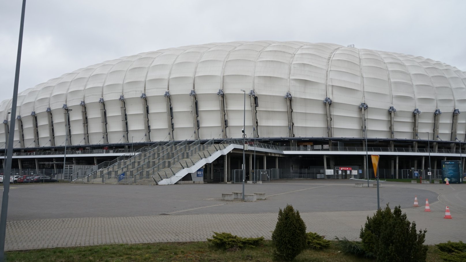 Zdjęcie stadionu, w centrum schody prowadzące do wewnątrz budynku, na pierwszym planie rośliny