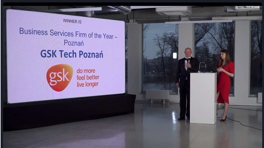 Ceremonia ogłoszenia laureatów konkursu CEE Business Services Summit&Awards. Na zdjęciu osoby prowadzące galę oraz ekran, na który wyświetlono nazwę laureata w kategorii poznańska firma roku z sektora usług biznesowych - GSK Tech Poznań.