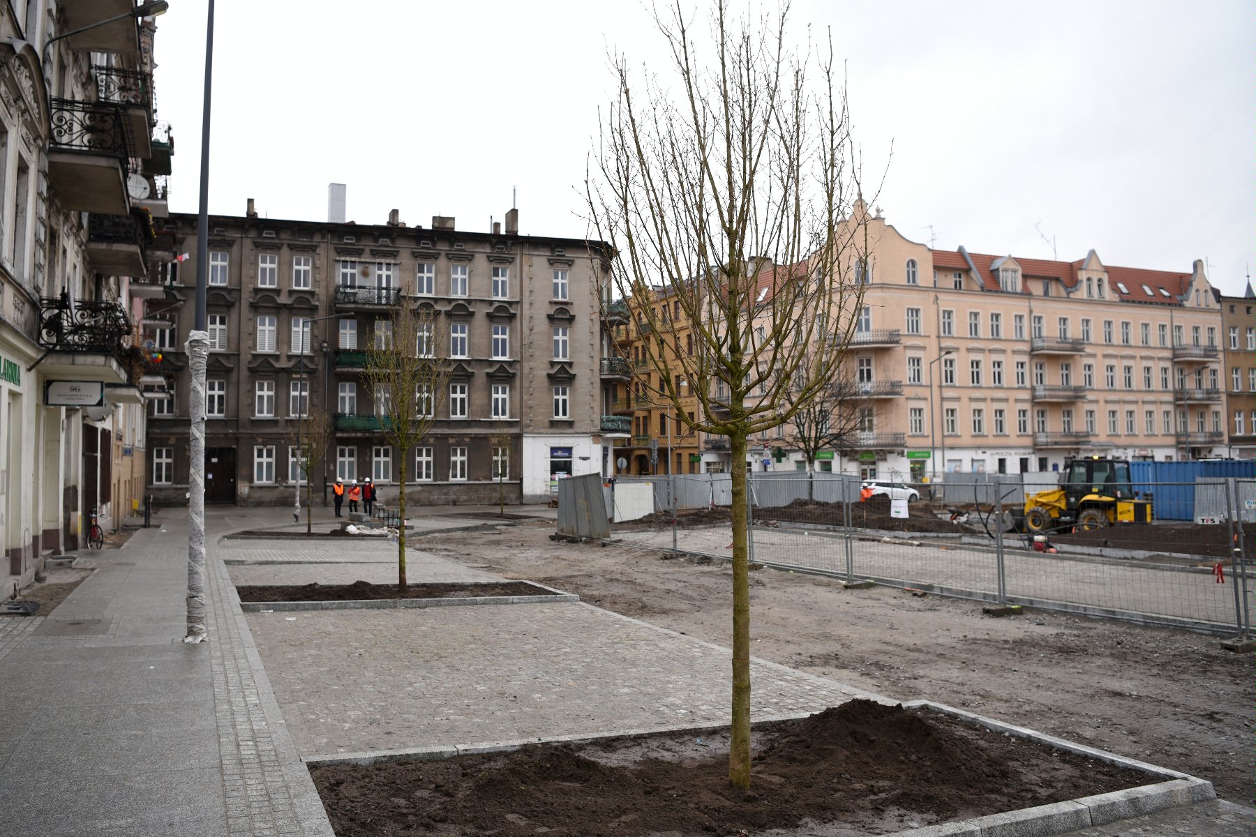 Rynek Łazarski, na pierwszym planie nowe drzewa i przechodnie, w tle plac budowy - grafika rozmowy