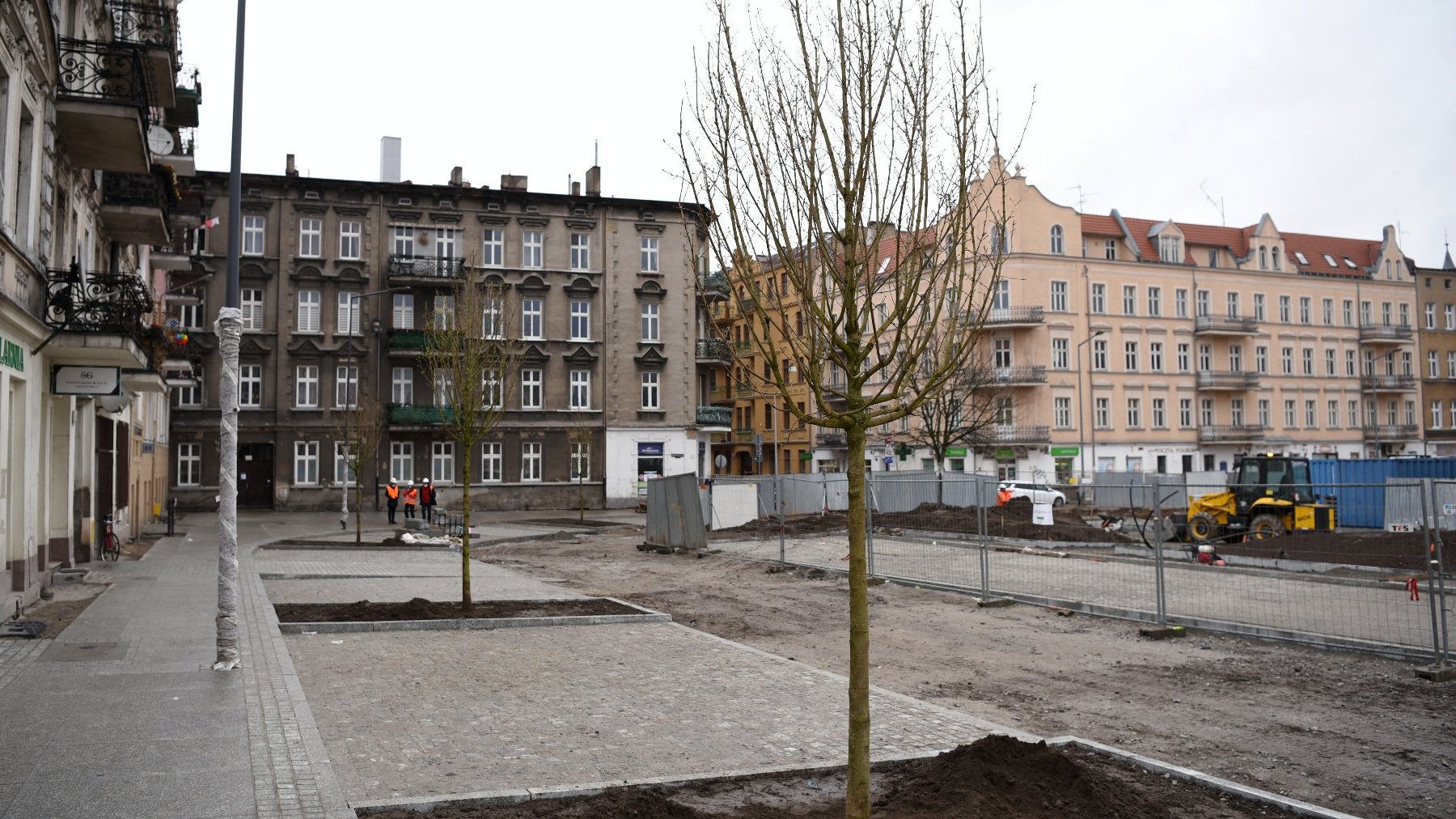 Rynek Łazarski, na pierwszym planie nowe drzewa i przechodnie, w tle plac budowy