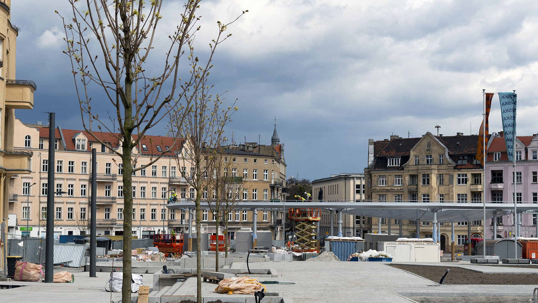 Na zdjęciu rynek, w tle konstrukcja zadaszenia, przy której pracują robotnicy, na pierwszym planie nowo nasadzone drzewa