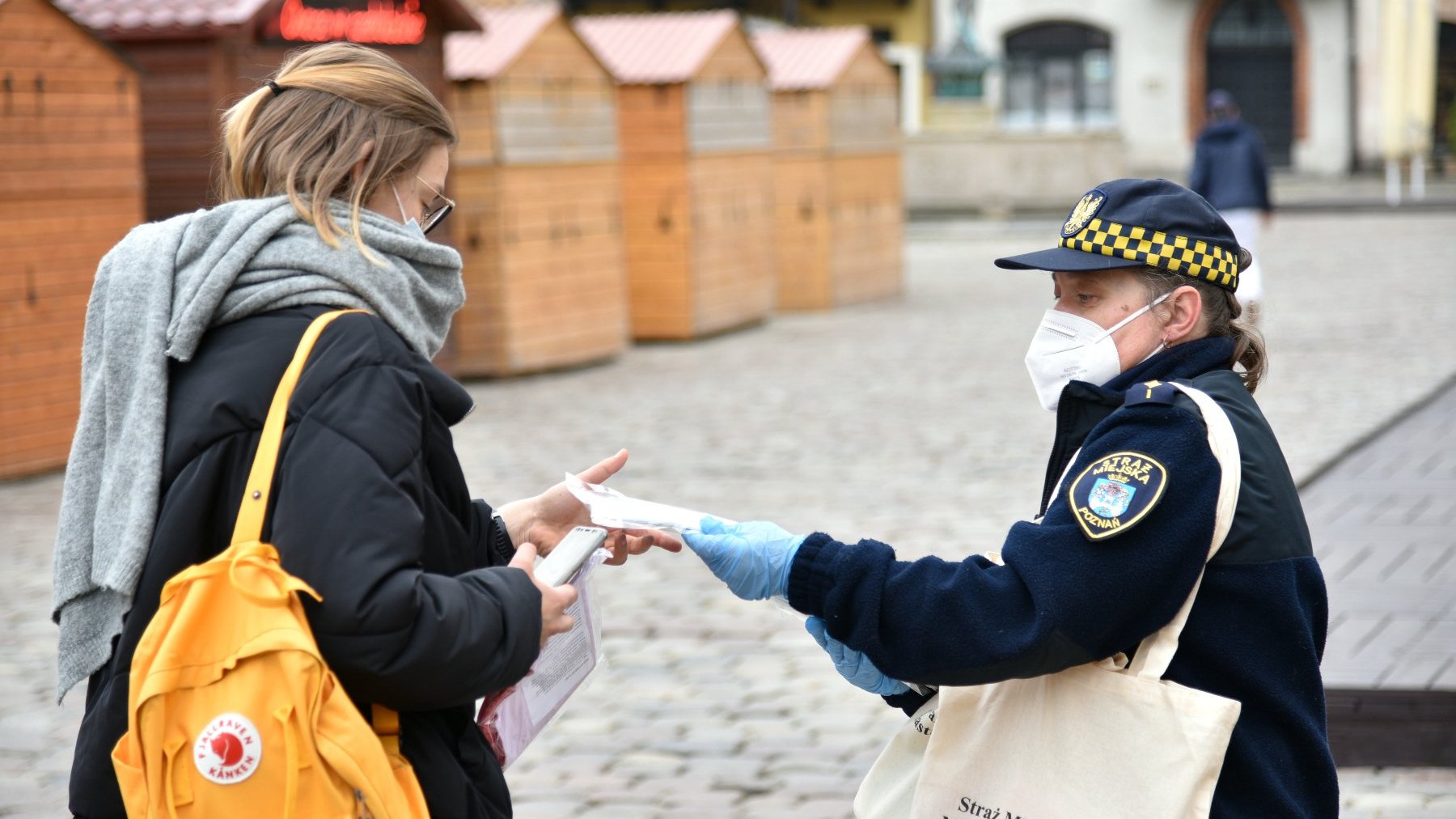 Galeria zdjęć przedstawia strażniczki miejskie rozdające mieszkańcom biało-czerwone flagi.