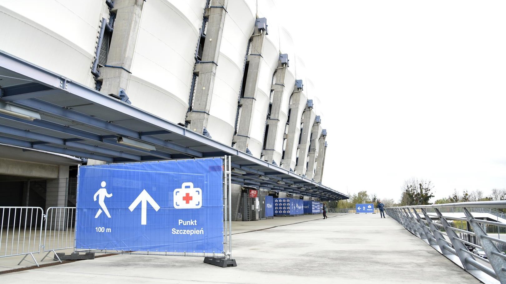 Stadion z zewnątrz, na pierwszym planie baner informujący o tym, jak dojść do punktu szczepień