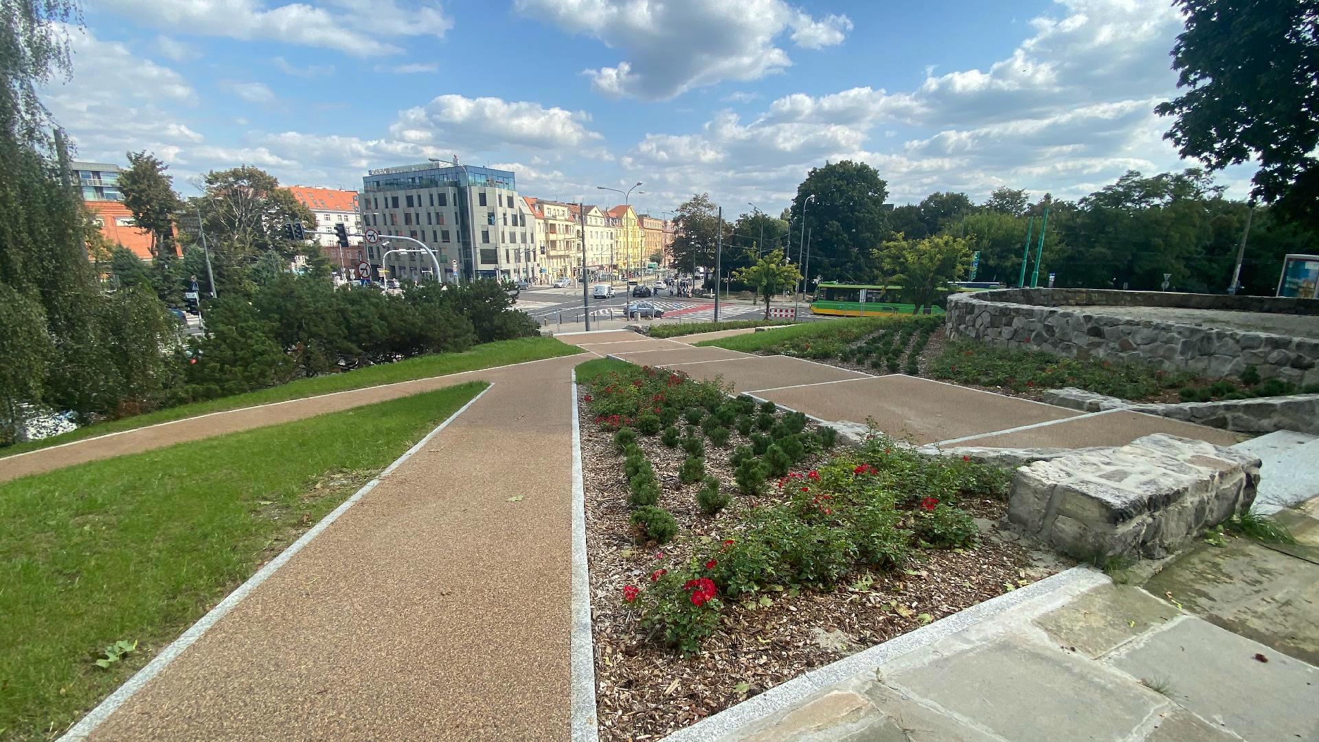 Zdjęcie przedstawia park. Widać na nim alejki spacerowe oraz roślinność. W tle znajdują się budynki oraz jezdnia, po której jadą samochody i tramwaje. - grafika rozmowy