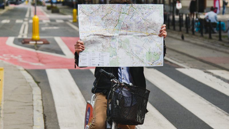 Mężczyzna na rowerze w centrum miasta, w rękach trzyma mapę