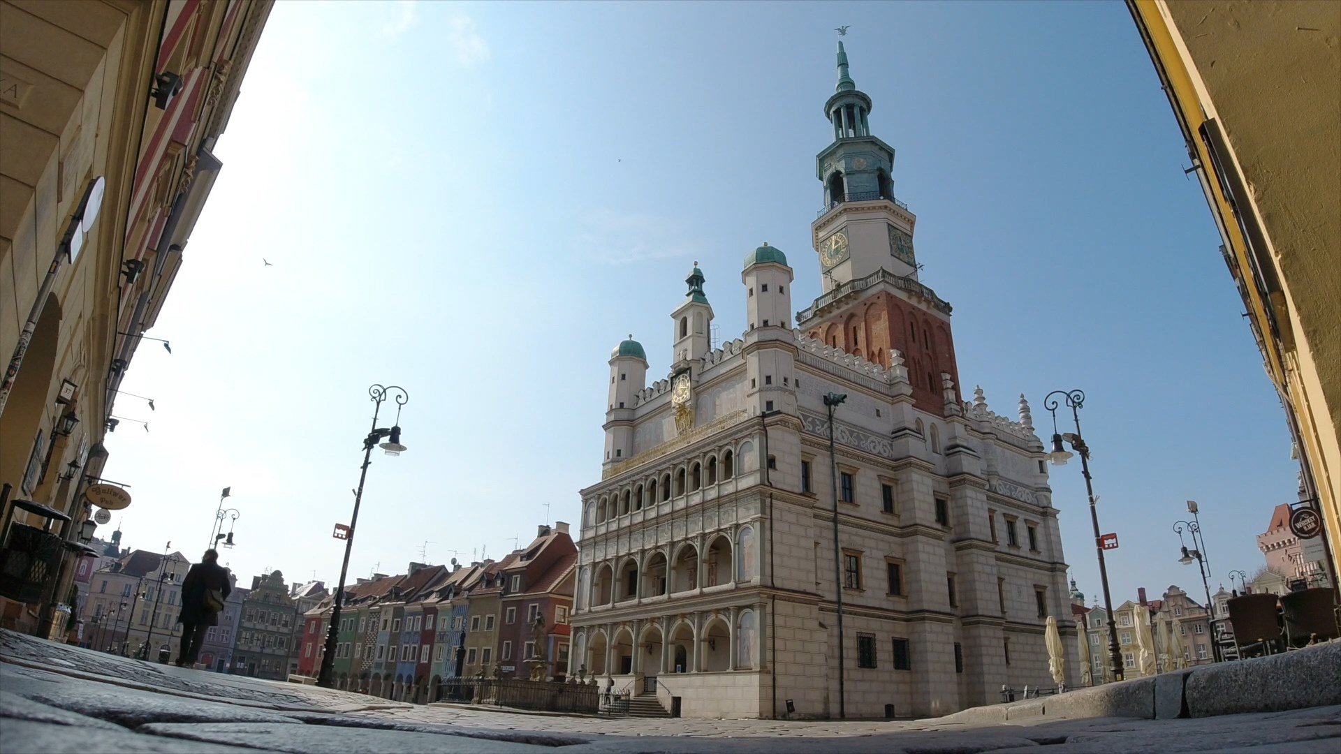 Na zdjęciu Ratusz na Starym Rynku widziany z żabiej perspektywy, w tle domki budnicze i przechodzień