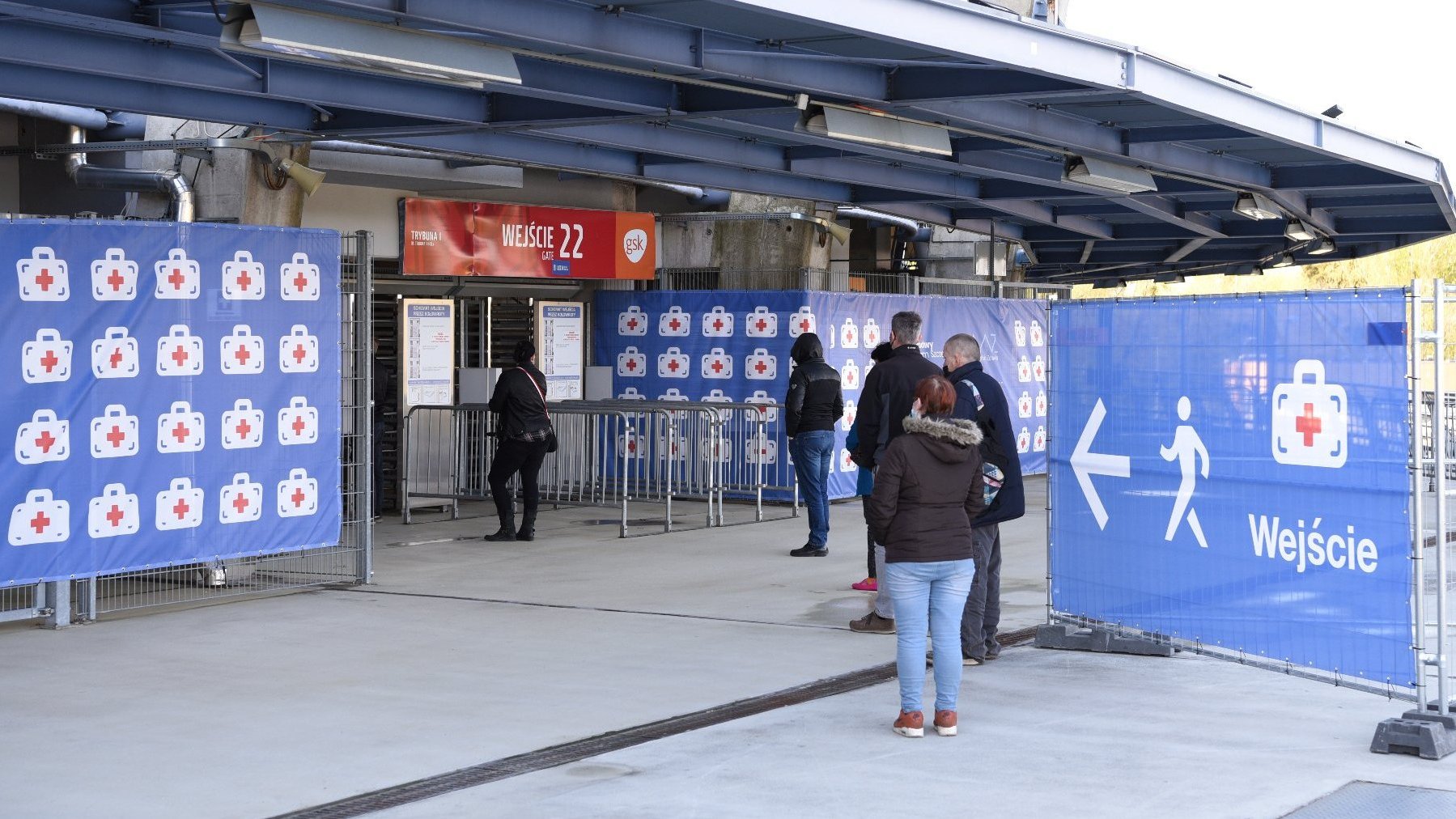 Zdjęcie przedstawia punkt szczepień z zewnątrz, przed wejściem czeka kilka osób