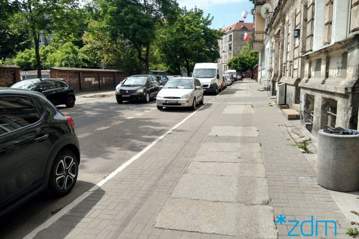 Zdjęcie przedstawia jezdnię i chodnik. Na poboczu drogi stoją zaparkowane samochody. - grafika rozmowy