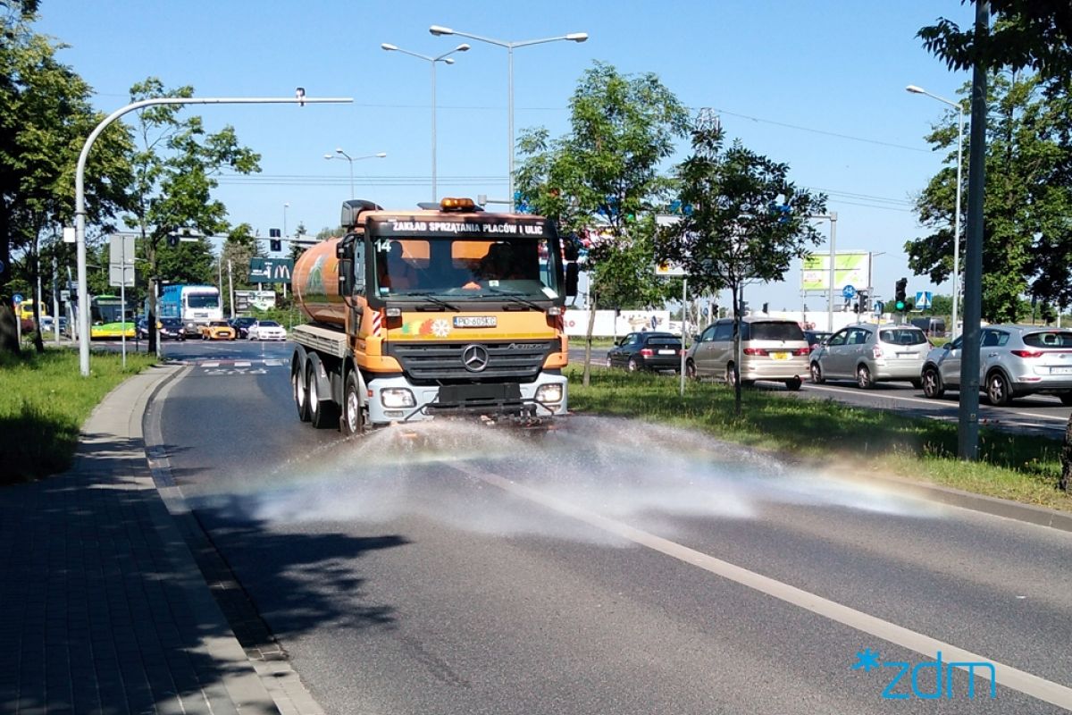 Zdjęcie przedstawia samochód polewaczkę, jadący po ulicy. - grafika rozmowy