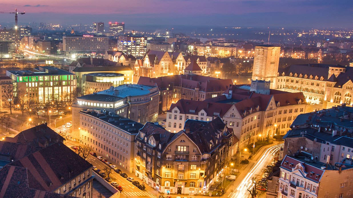 Grafika: panorama Poznania po zachodzie słońca, na pierwszym planie kamienice, w tle CK Zamek - grafika rozmowy