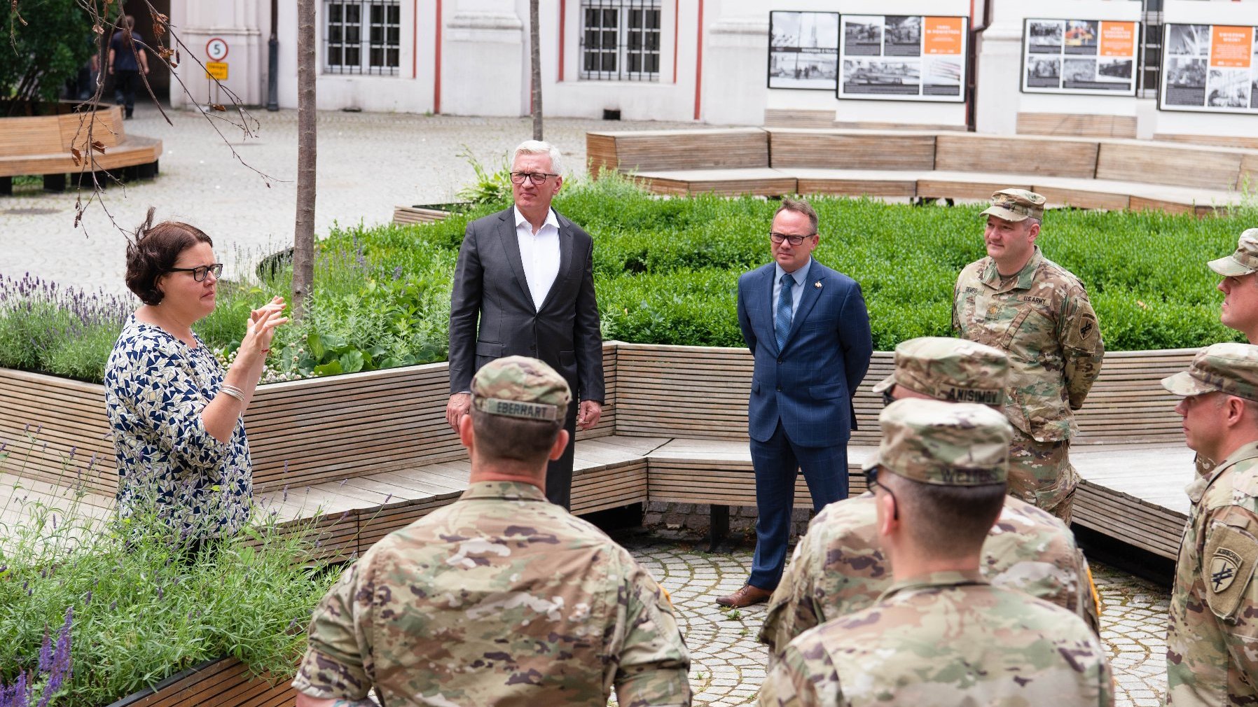 Dziedziniec Urzędu Miasta Poznania. Na nim 6 mężczyzn w mundurach i dwóch w garniturach: Jacek Jaśkowiak i Scott Brokaw. Obok gestykulująca kobieta