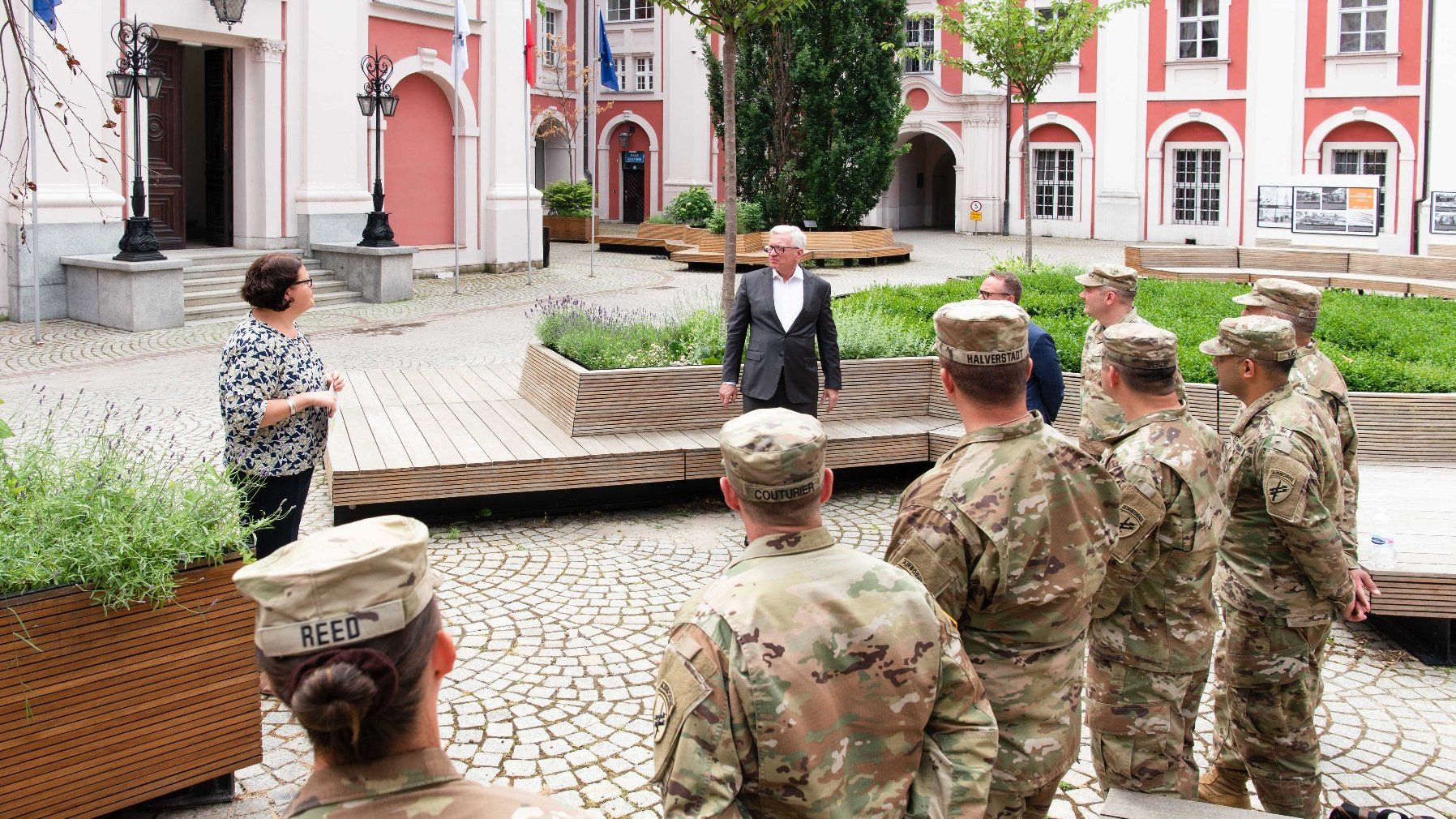 Dziedziniec Urzędu Miasta Poznania. W centrum Jacek Jaśkowiak, obok kobieta. Przed nimi, w grupie, stoją żołnierze w mundurach