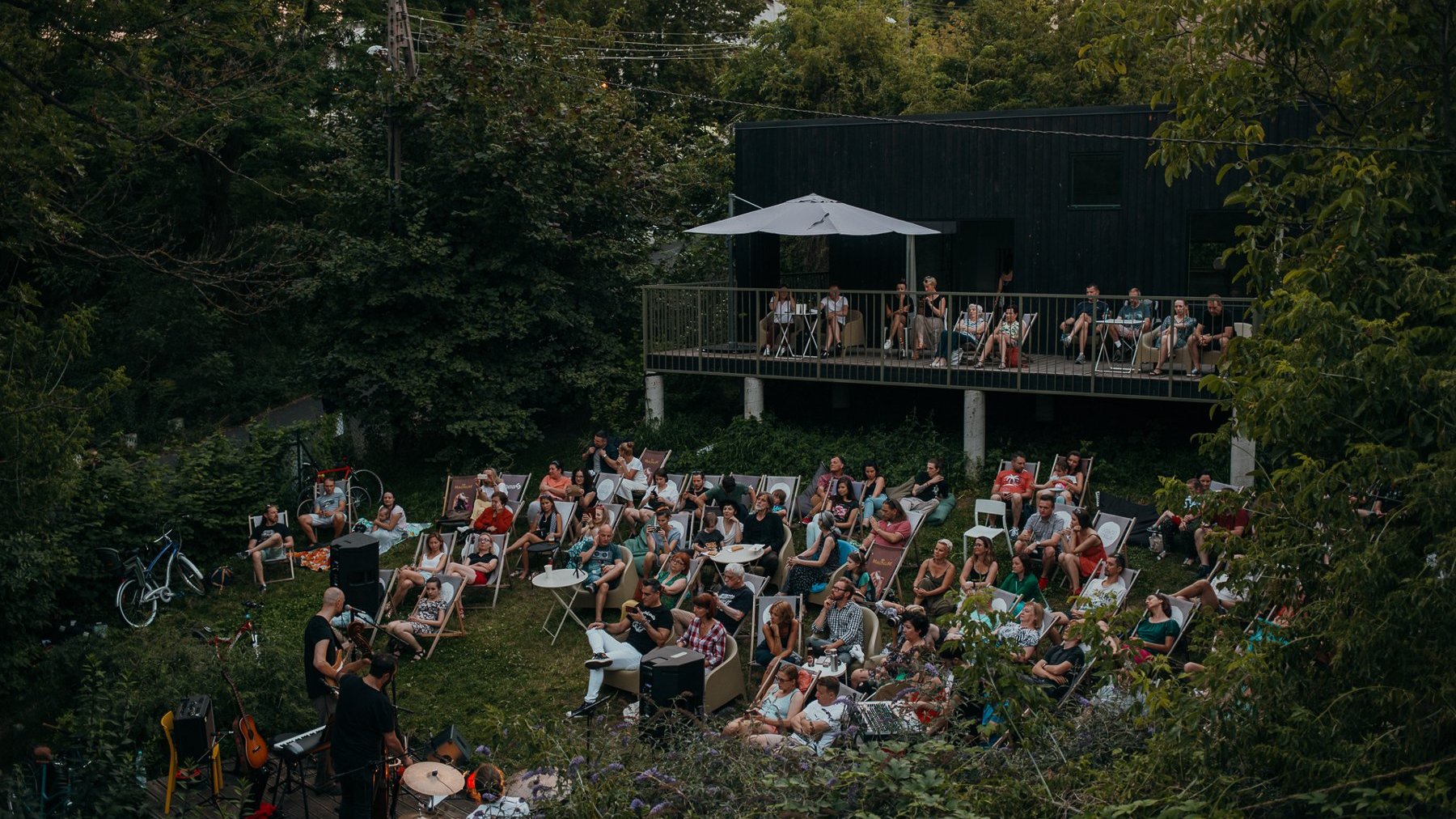 Zdjęcie Szeląga: kameralny koncert. Grupa ludzi na leżakach, w otoczeniu zieleni słucha dwóch muzyków