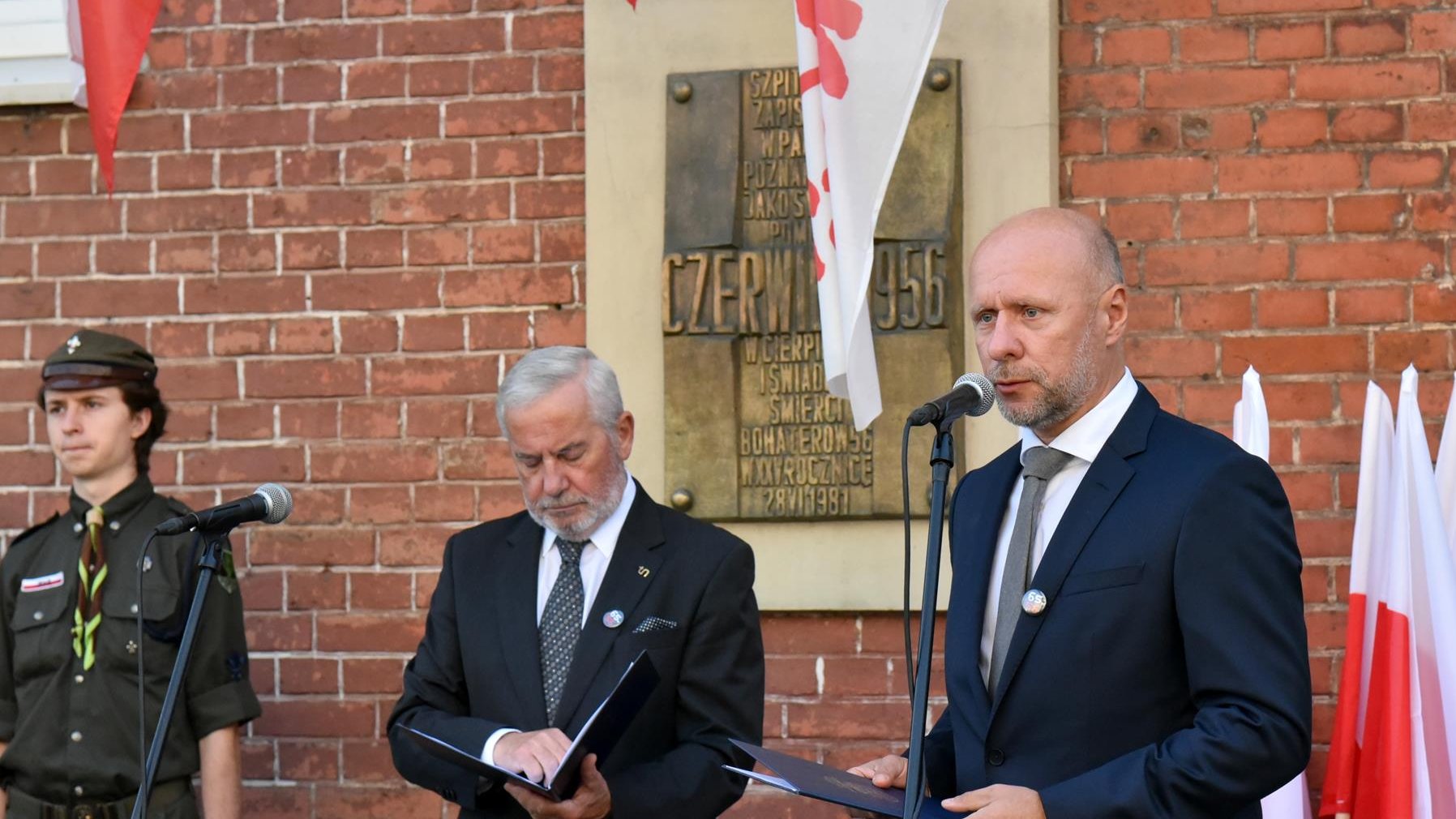 Bartosz Guss, zastępca prezydenta Poznania przy mikrofonie, za nim tablica poświęcona bohaterom Czerwca '56, obok konferansjer i harcerka