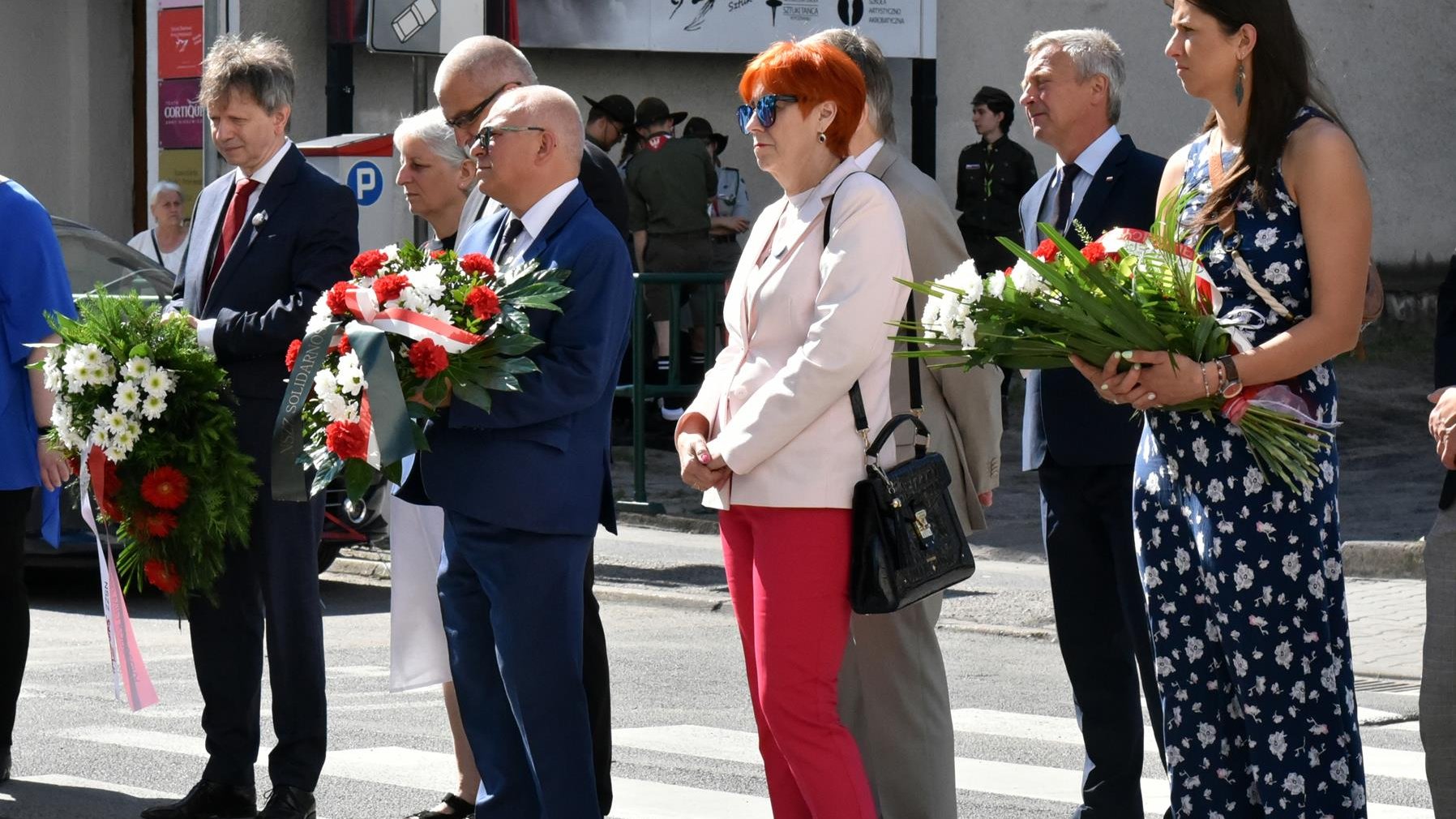 Grupa ludzi składających kwiaty, stojących w rzędzie