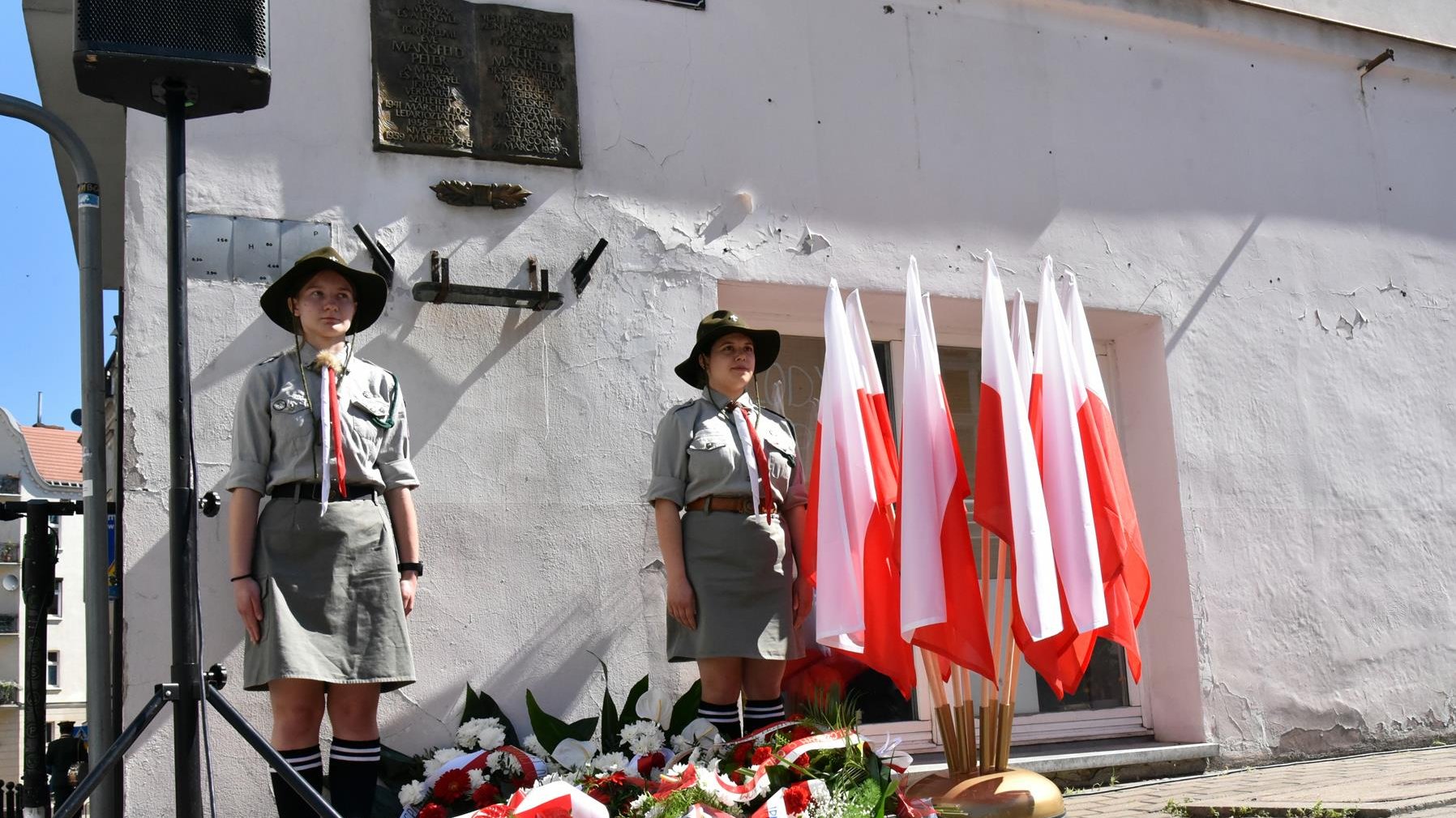 Tablica pamięci Petera Mansfelda, po obu stronach harcerki, obok polskie flagi, pod tablicą kwiaty