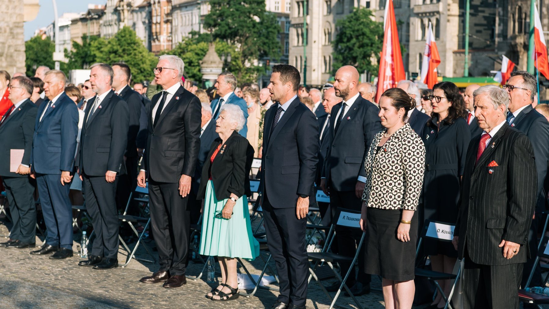 Grupa samorządowców - wśród nich Jacek Jaśkowiak - stojąca w rzędzie na placu Adama Mickeiwicza, za nimi polskie flagi, w centrum Aleksandra Banasiak