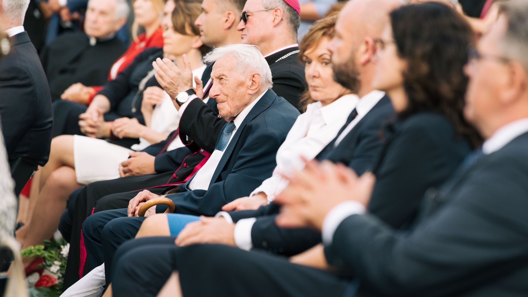 Grupa ludzi siedzących w rzędzie, wśród nich starszy pan - Zenon Wechmann