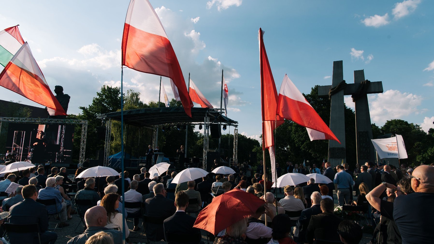 Tłum ludzi na placu Adama Mickiewicza, na pierwszym planie flagi, w tle pomnik