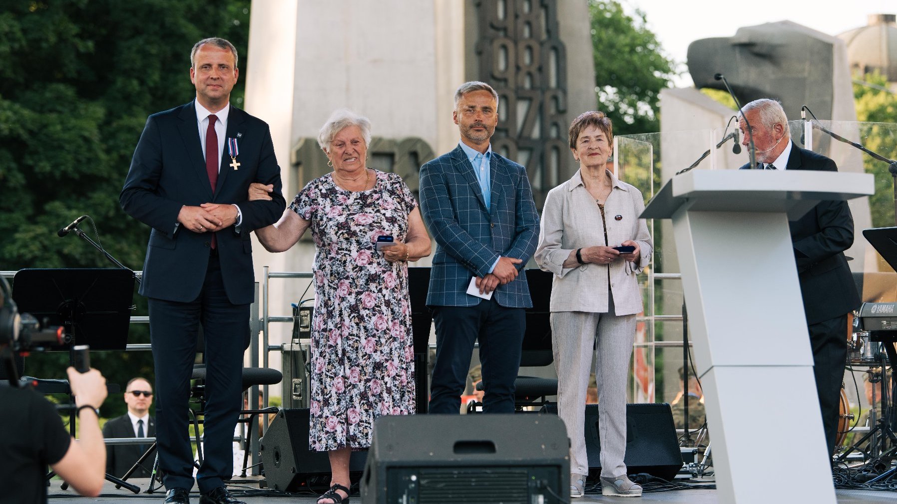 Plac Mickiewicza, grupa osób na scenie, w tle Pomnik Poznańskiego Czerwca