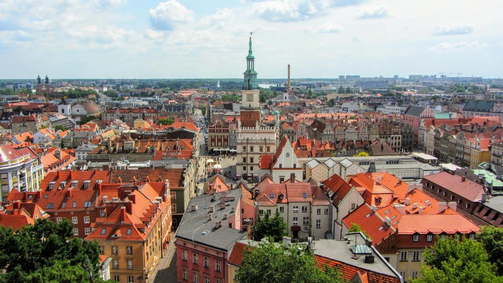 Panorama Poznania, na pierwszym planie dachy kamienic, w centrum wieża Ratusza, u góry błękitne niebo, na nim białe chmury