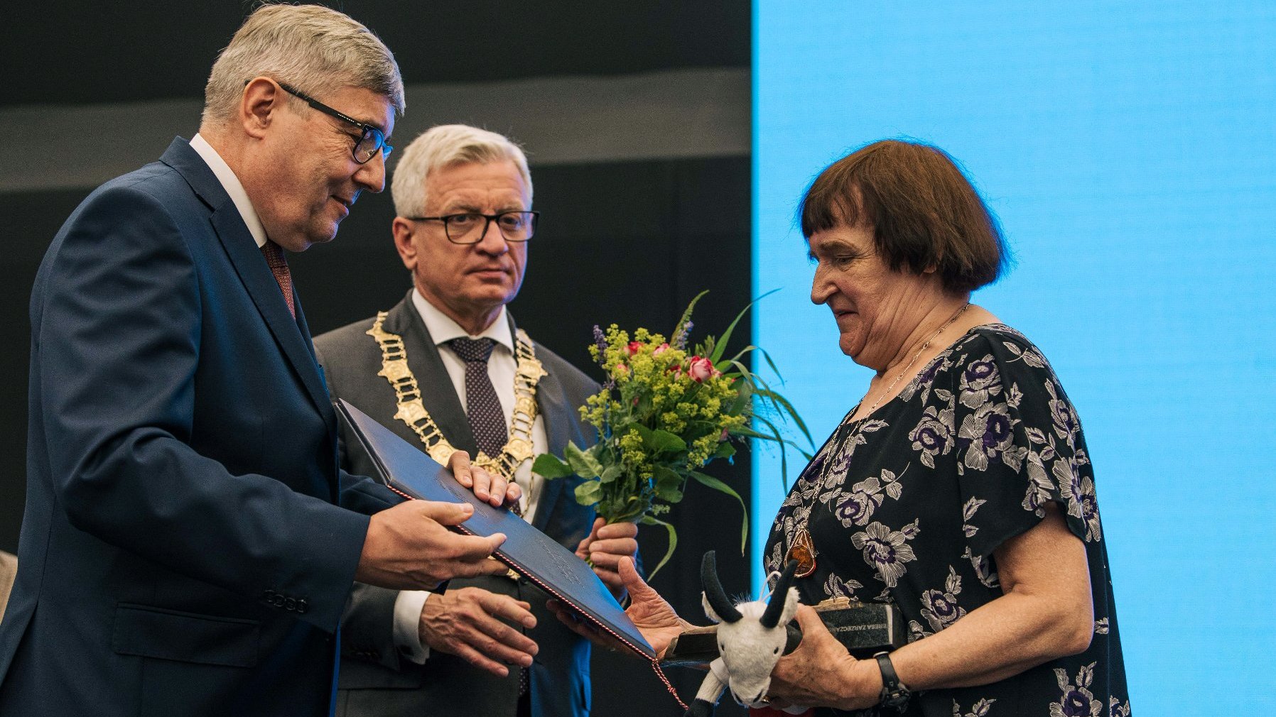 Kobieta odbierająca nagrodę z rąk Grzegorza Ganowicza, za nią Jacek Jaśkowiak trzymający kwiaty