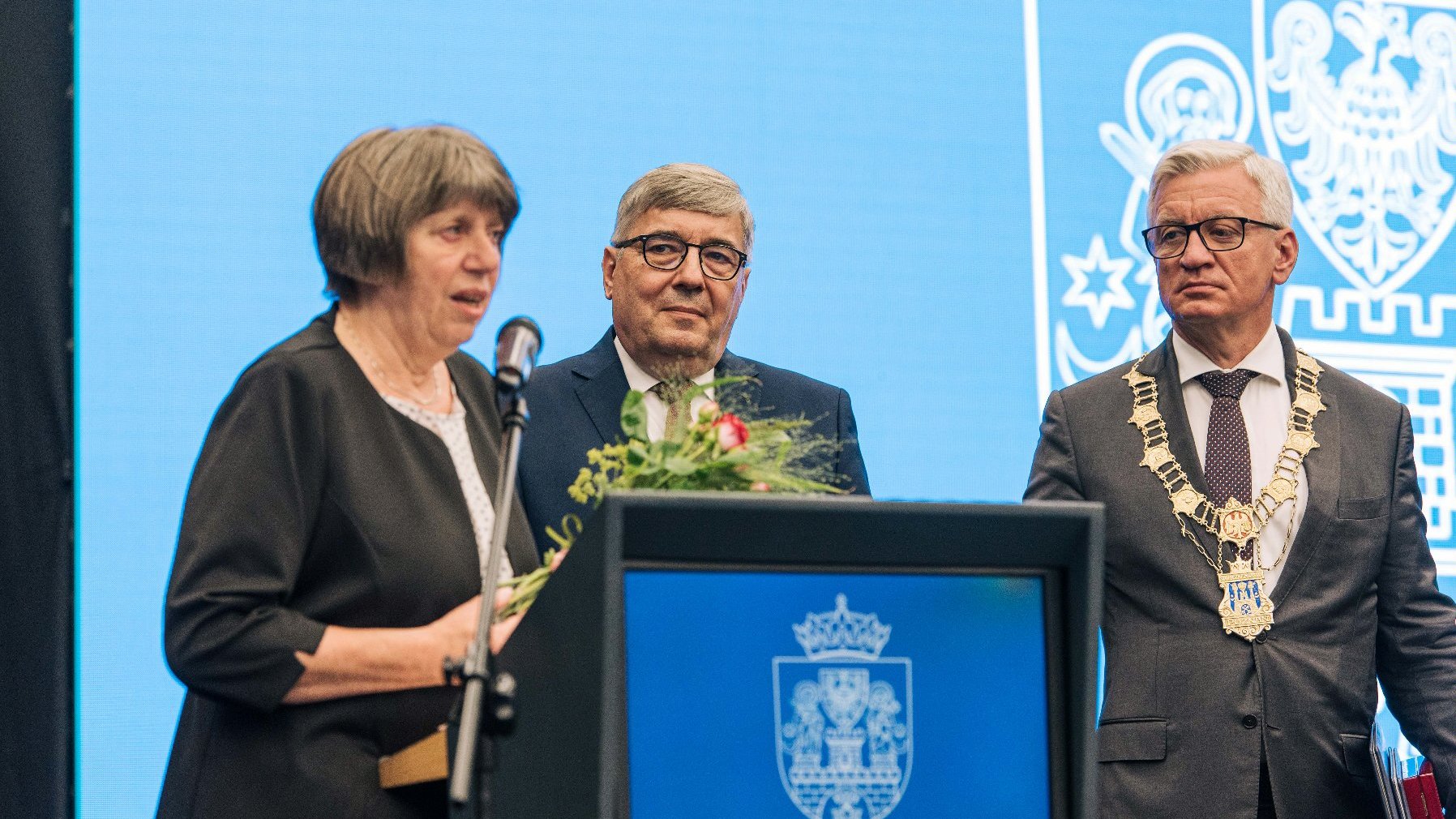 Kobieta - Barbara Napieralska - przy mównicy, za nią Jacek Jaśkowiak i Grzegorz Ganowicz